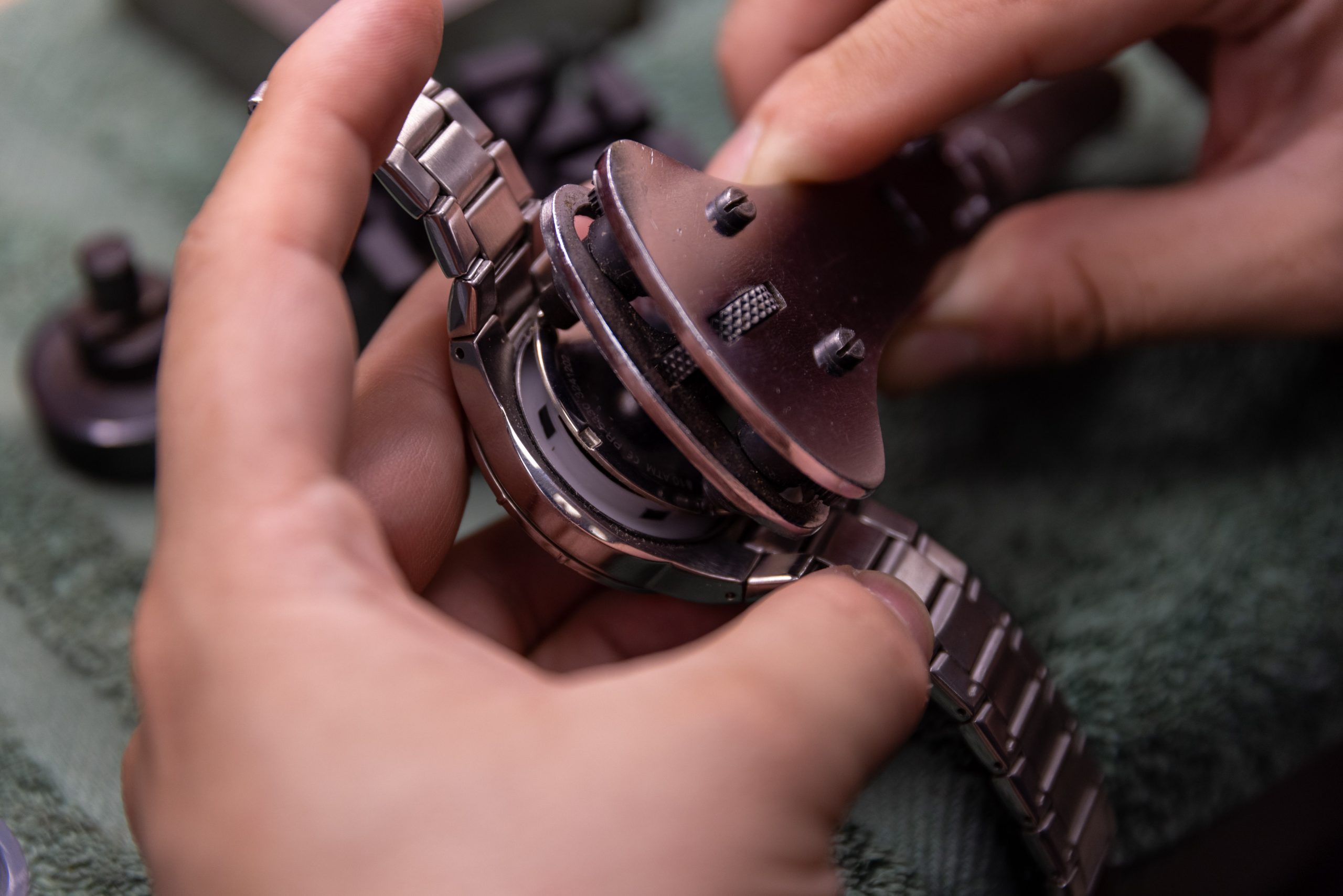 Hands work on a watch mechanism at a repair bench.