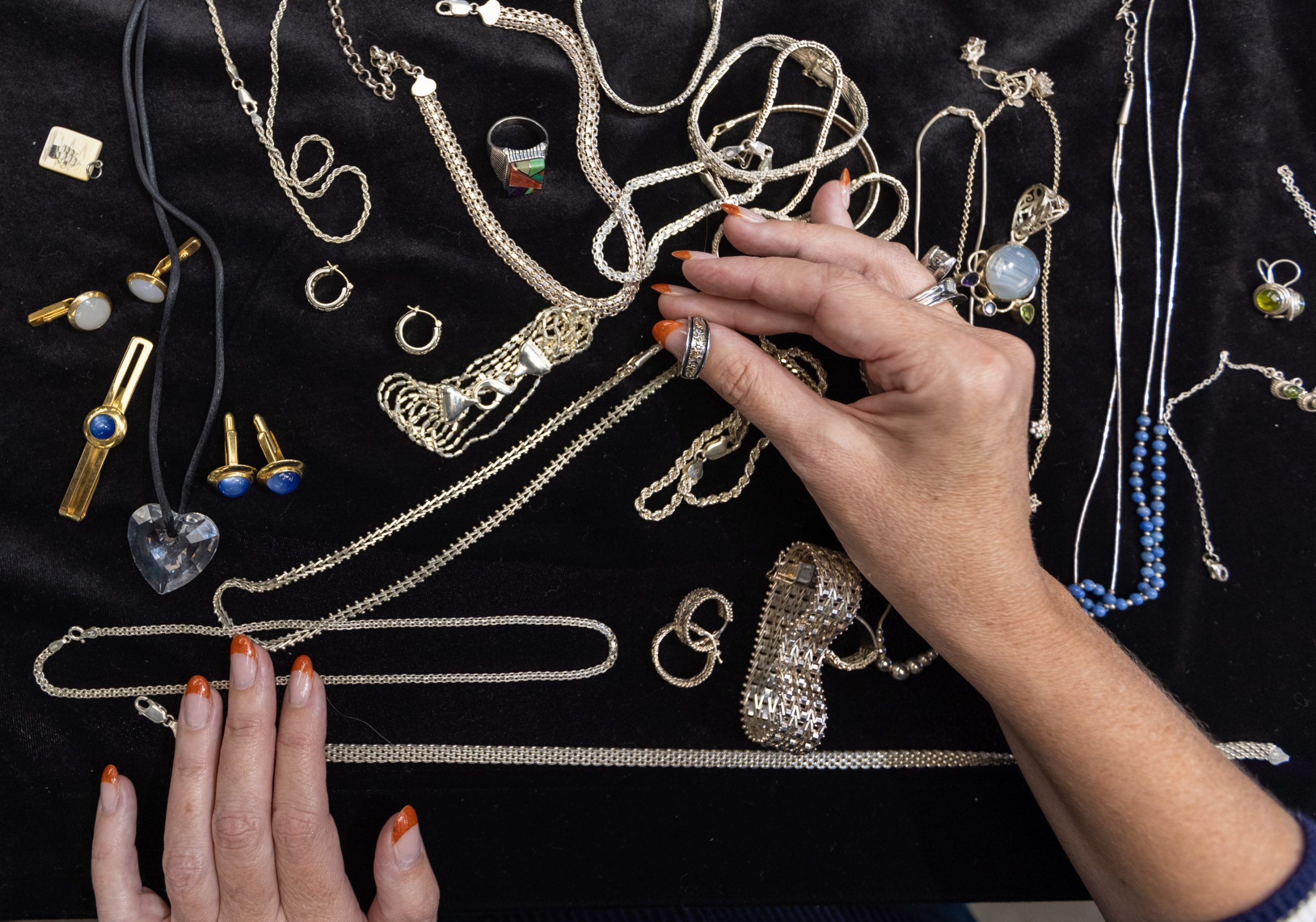 A hand examines a necklace among jewelry arranged on a dark surface.