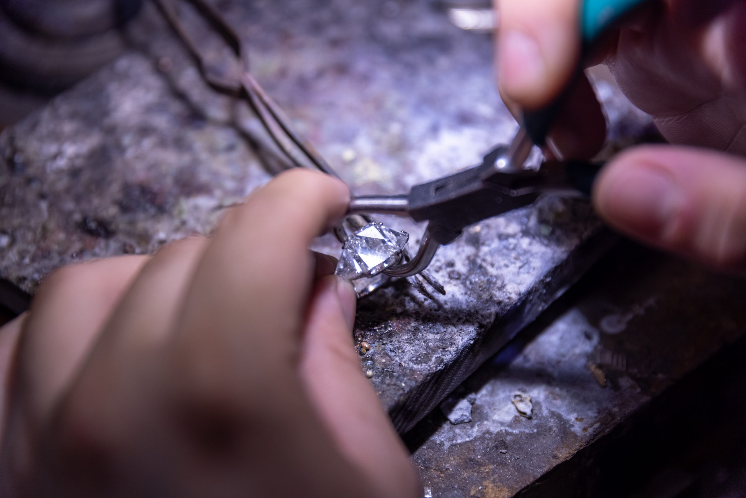 Hands perform detailed work on jewelry at a repair bench.
