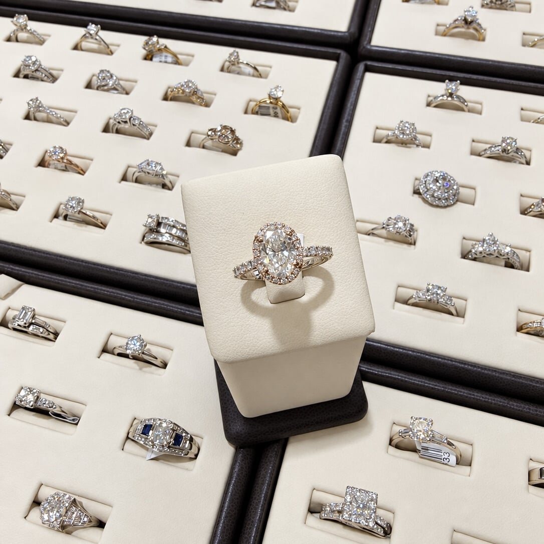 An oval halo estate engagement ring on an ivory stand surrounded by rings in display trays.