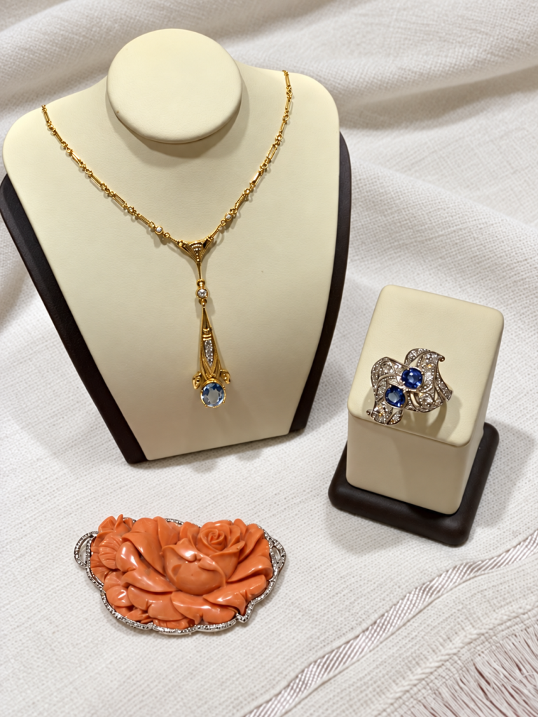Estate jewelry display featuring a gemstone pendant necklace, a blue floral ring, and a carved coral rose brooch.