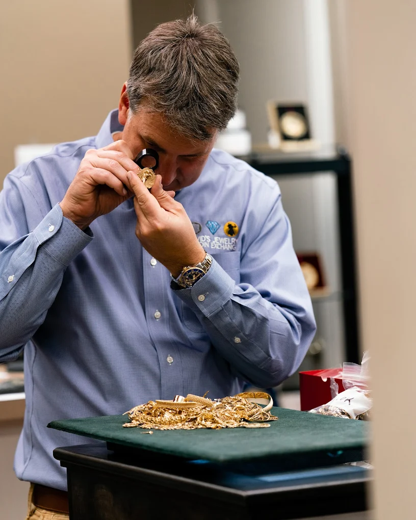 A team member examines jewelry with a jeweler’s loupe at the showroom counter.