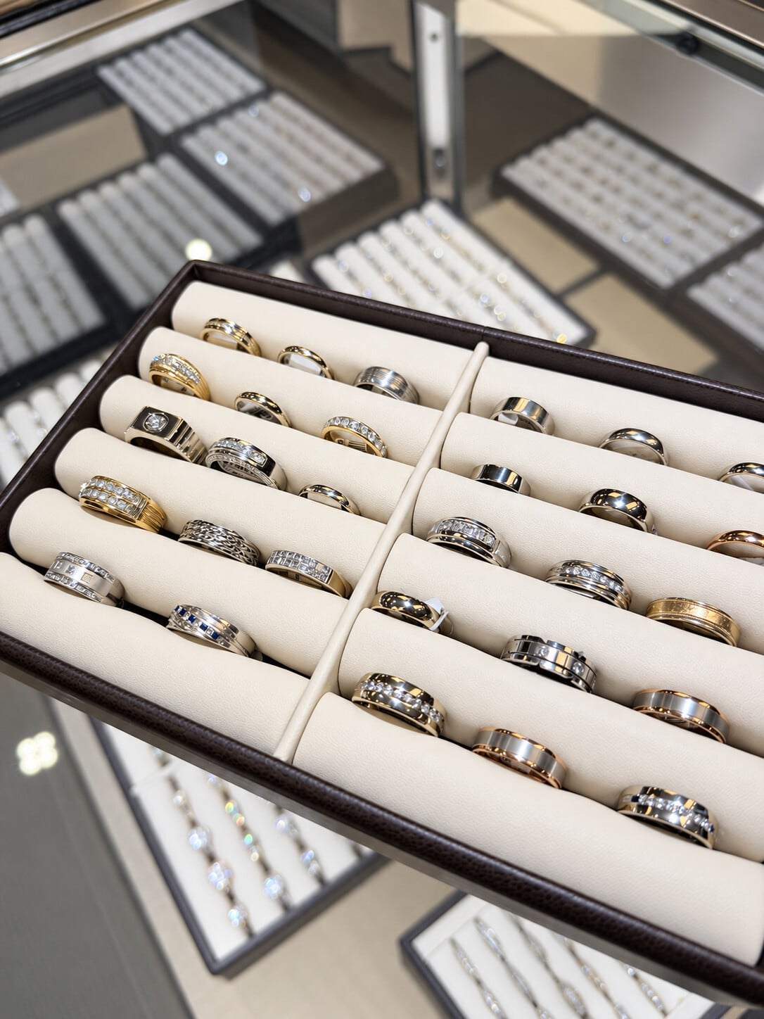 Men’s rings and wedding bands in polished, textured and stone-set designs on an ivory display tray.